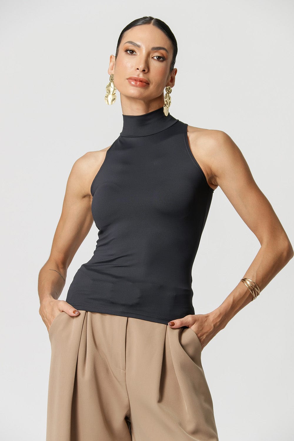 Woman wearing a black sleeveless top and beige pants against a light gray background